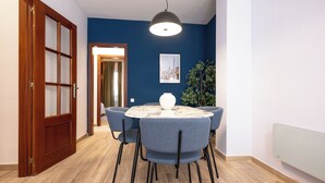 A dining area with a round table, four chairs, a vase, and a hanging light fixture.