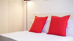 A bed with white bedding and two red pillows, a bedside lamp, and a white wardrobe.