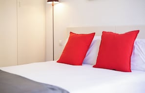 Een bed met witte beddengoed en twee rode kussens, een bedlampje en een witte garderobe.