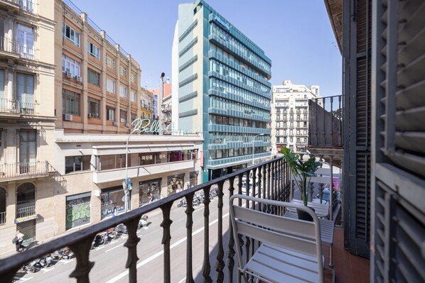 Un balcón con barandilla metálica que da a una calle con scooters estacionados y edificios.