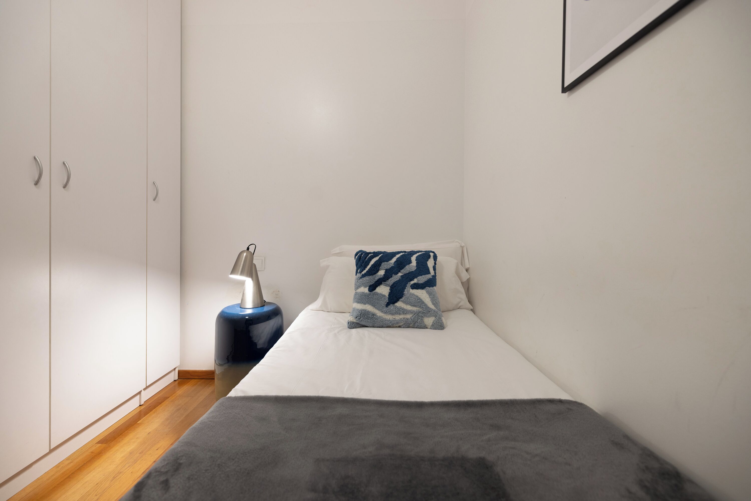 Een slaapkamer met een bed, nachtkastje, lamp en een kledingkast.