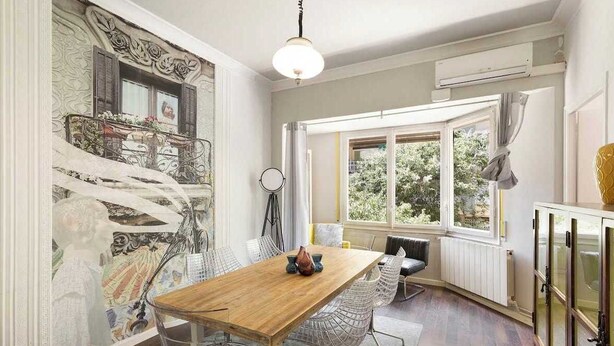 A dining area with a wooden table, clear chairs, and a large window with a view of greenery.