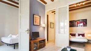 Habitación de hotel moderna con una cama blanca, un escritorio con computadora, un televisor y un cuadro en la pared.