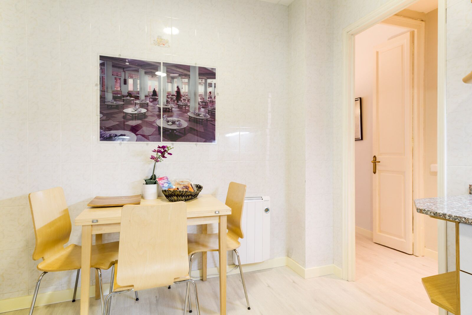 A dining area with a table set for four, a vase with flowers, and a wall-mounted picture.