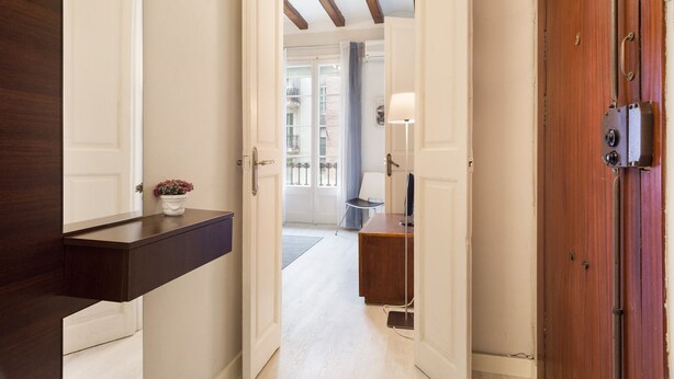 Un pasillo con un banco de madera oscura, una puerta blanca y una puerta de madera con manija metálica.