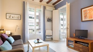Una sala de estar con sofá, mesa de centro, televisor y balcón con una silla.