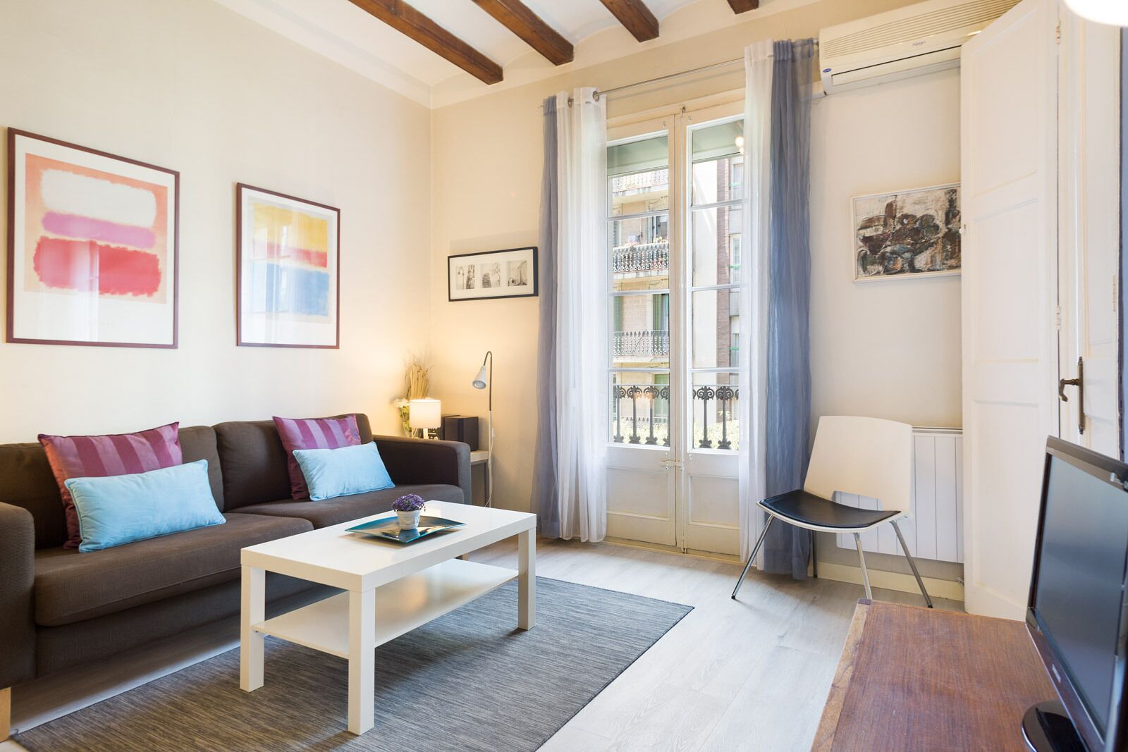 Ein modernes Wohnzimmer mit einer Couch, einem Couchtisch und einem Fernseher. An den Wänden hängen zwei gerahmte Kunstwerke, eine Lampe und ein Sessel.