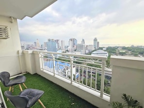 Enjoy the city view from this balcony with a railing and artificial grass, featuring two chairs for a comfortable seating area.