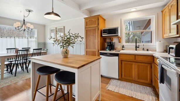 A modern kitchen with wooden cabinets, a central island with stools, a built-in microwave, and a dining area with a chandelier.