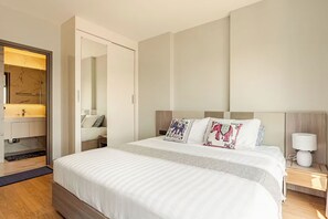 A modern hotel room with a large bed, a bedside table with a lamp, and a wardrobe with a mirror.