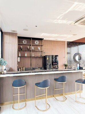 A modern bar area with a wooden counter, bar stools, and a decorative mirror.