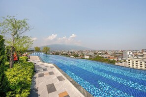 A swimming pool with a tiled pattern, surrounded by greenery and a cityscape in the background.