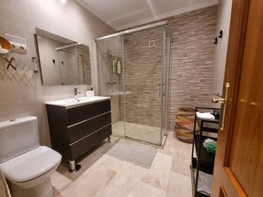 Ein modernes Badezimmer mit einer gläsernen Duschkabine, einer weißen Toilette und einem schwarzen Waschtisch mit Spiegel.