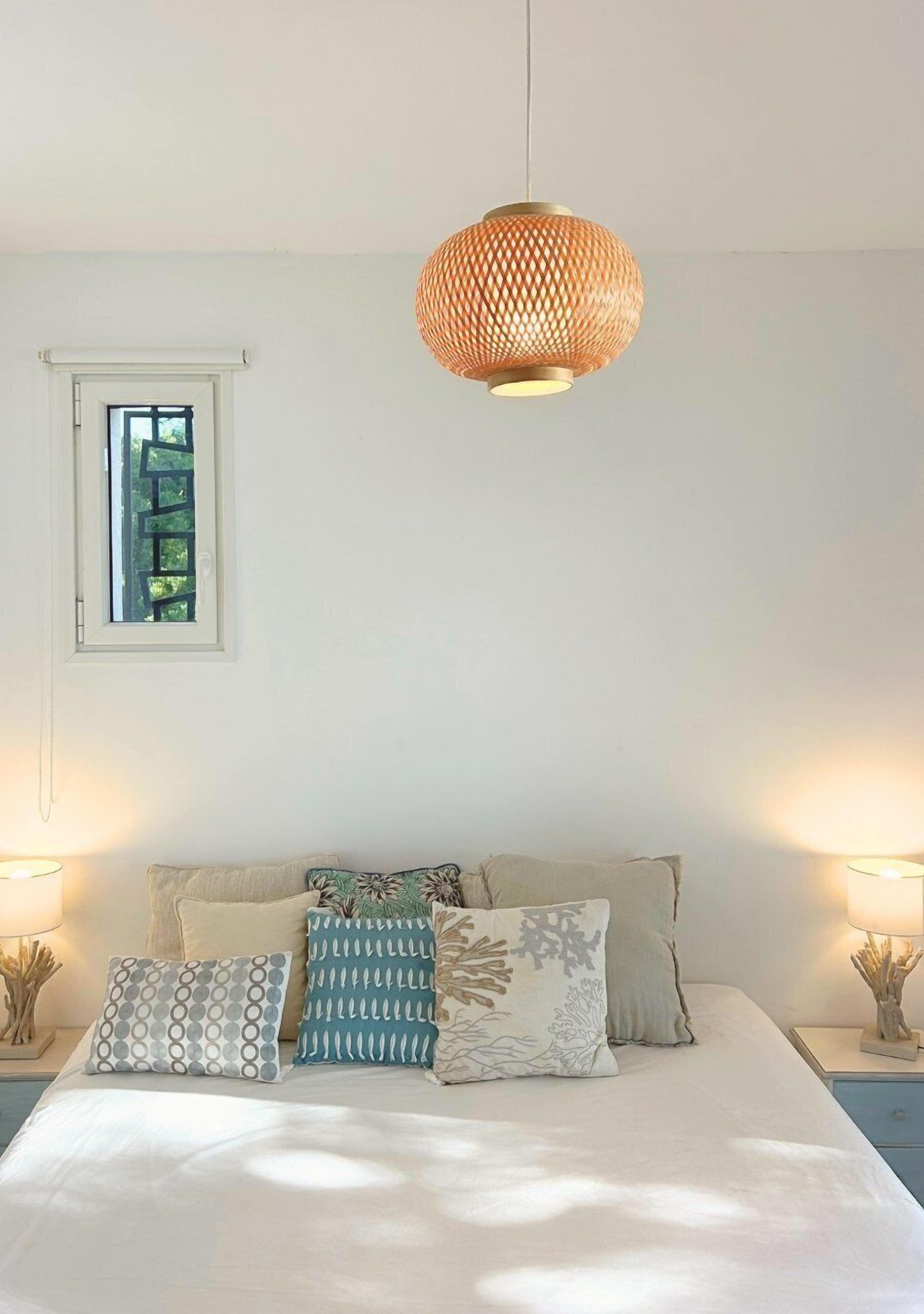 A bedroom with a bed, patterned pillows, bedside lamps, and a hanging light fixture.