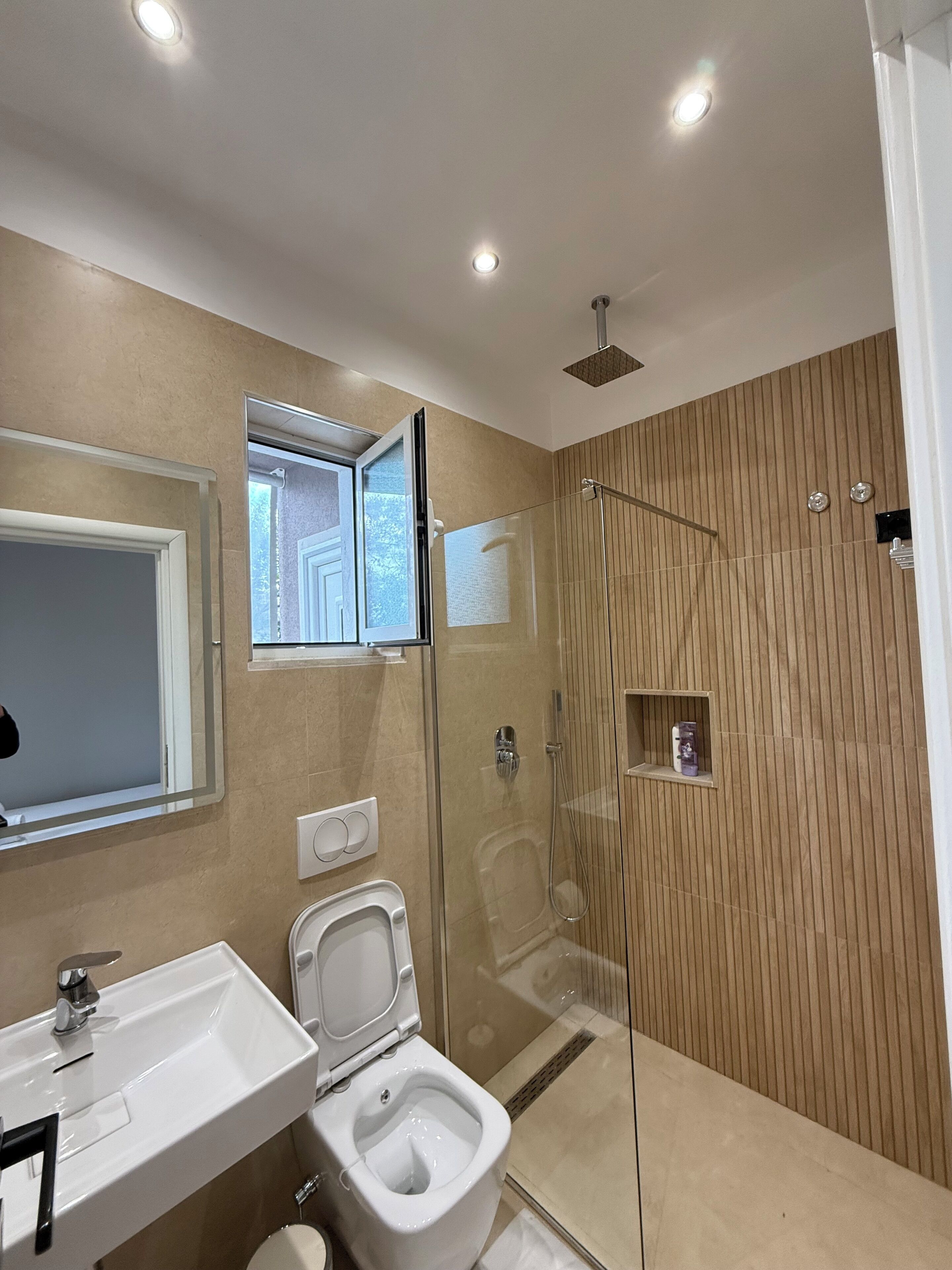 A modern bathroom with a glass-enclosed shower, a toilet, and a sink.