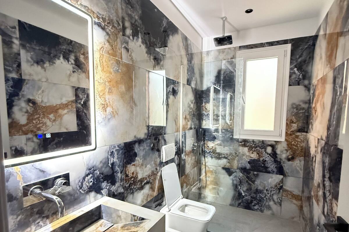 A modern bathroom with a marble backsplash, a large mirror, a sink, and a toilet.