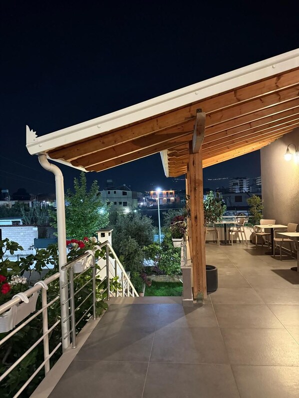 Ένας σκεπαστός εξωτερικός χώρος με πέργκολα, καθιστικά και θέα στην πόλη τη νύχτα.