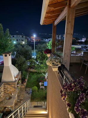 Μια ταράτσα με τζάκι από πέτρα, υπαίθριο καθιστικό και θέα στην πόλη τη νύχτα.