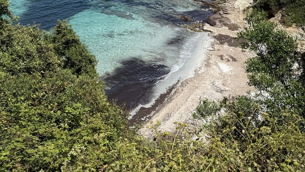A coastal landscape with clear blue waters, rocky shorelines, and dense greenery.