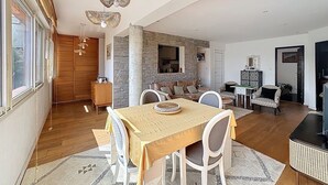 A spacious living area with a dining table, white chairs, and a stone accent wall.