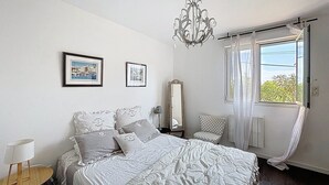 A bedroom with a large bed, a chandelier, a chair, and a window with curtains.