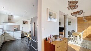 A modern kitchen with white cabinetry, a stainless steel refrigerator, and a dining area with a wooden table and chairs.