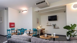 A modern hotel lobby with grey sofas, teal chairs, a wooden table, and a flat-screen TV on the wall. - Nobia 3 (Athens)