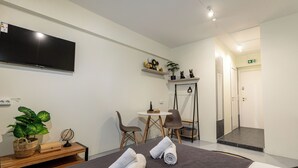 A hotel room with a bed, a desk, a chair, a TV, and a small table with a plant and decorative items. - Nobia 3 (Athens)