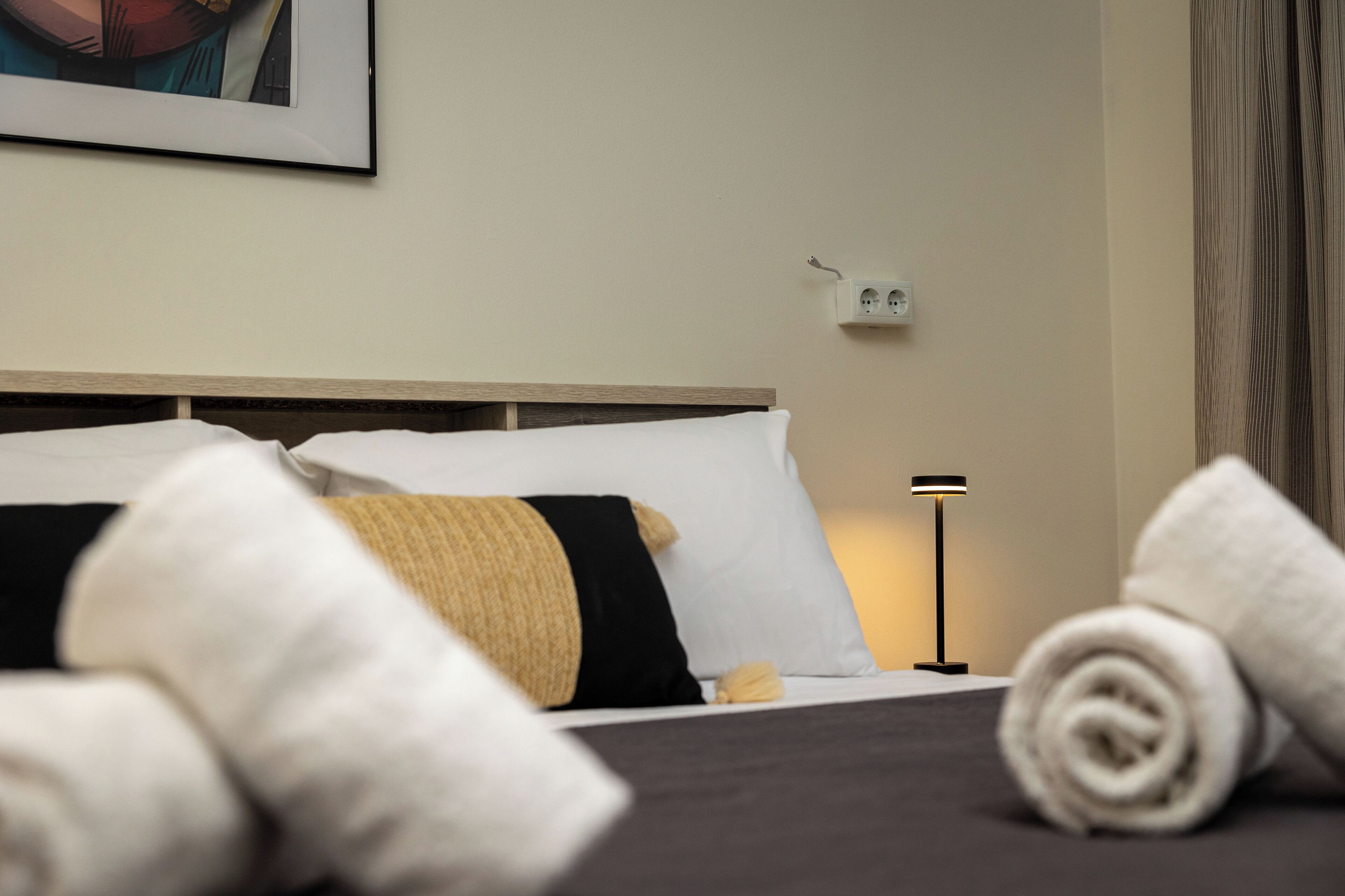 A neatly made bed with white and black bedding, a yellow pillow, and a rolled towel on the side.