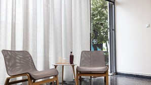 A modern room with two chairs, a small table, and a large window with a view of trees. - Nobia 3 (Athens)