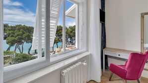 A room with a view of the sea, a desk, and a pink chair.