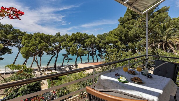 A balcony with a table set for breakfast overlooking a beach and pine trees.