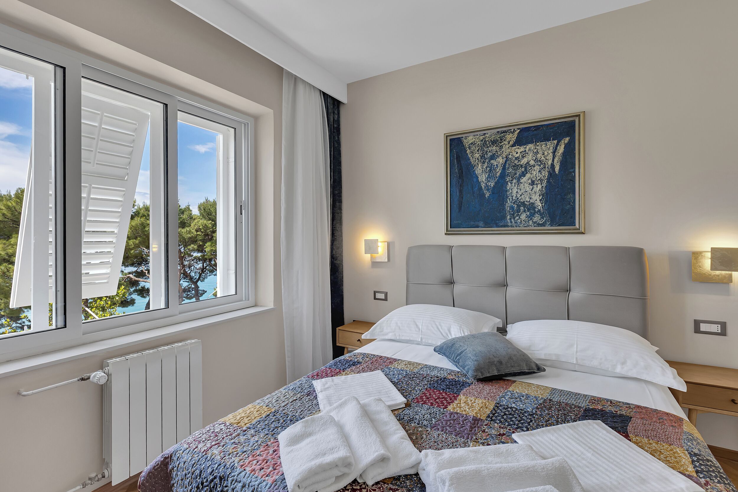 A neatly made bed with a colorful quilt, white pillows, and neatly folded towels.