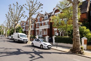 A residential street with houses, a white van, and a white car parked on the side. - The Secret Oasis, by Veeve (London)