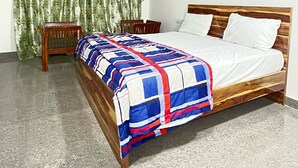 A bedroom with a wooden bed, a small bedside table, a green curtain, and a ceiling fan. - Hotel Mid Town (New Delhi)