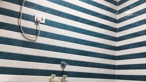 A bathroom with striped tile walls, a toilet, a sink, and a shower. - Hotel Mid Town (New Delhi)