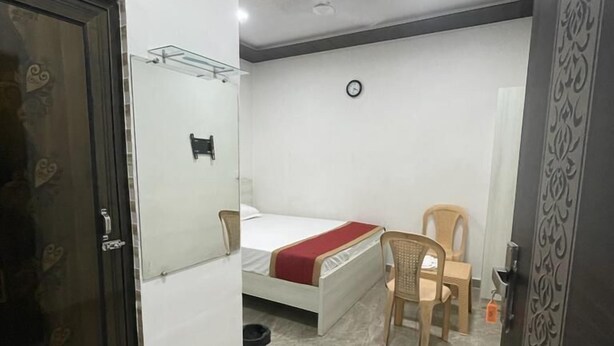 A compact room with a bed, a chair, a small table, and a clock on the wall. - Hotel Mid Town (New Delhi)