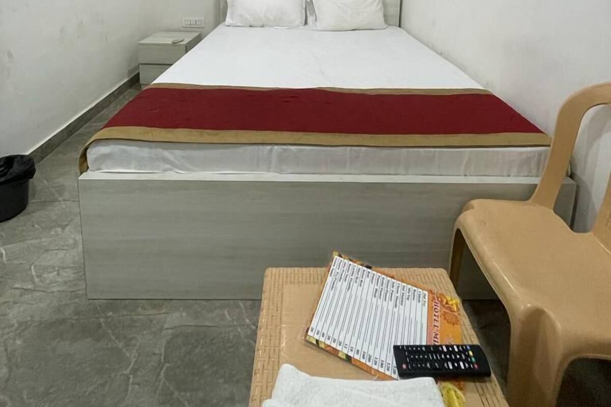 A hotel room with a bed, a nightstand, a chair, and a small table with a remote control and a menu.