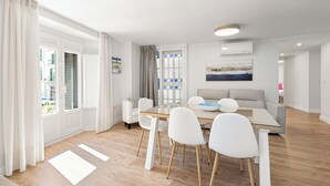 A modern living room with a glass dining table, white chairs, a grey sofa, and a painting on the wall. - Stay U-nique Apartment Plaza de la Merced (Málaga)