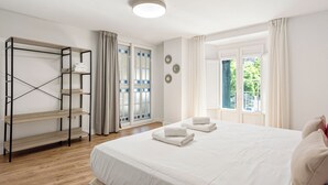 A bedroom with a large bed, a wooden shelf unit, and a window with curtains. - Stay U-nique Apartment Plaza de la Merced (Málaga)