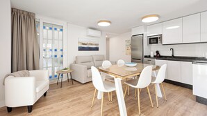 A modern living room with a sofa, a dining table with chairs, a kitchen area with appliances, and a large window with curtains. - Stay U-nique Apartment Plaza de la Merced (Málaga)