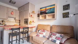 Eine moderne Küche mit Holzausstattung, einer roten Arbeitsplatte und einer hängenden Pendelleuchte. Es gibt ein Sofa mit Kissen in den Farben der britischen Flagge und ein Gemälde einer Brücke.