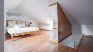 Ein Schlafzimmer mit einem hölzernen Bett, einem großen Spiegel und einer schrägen Decke.