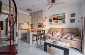 Une cuisine moderne avec des meubles en bois, un coin repas doté d’un comptoir rouge et un canapé agrémenté de plusieurs coussins.