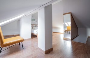 Une chambre mansardée avec un plafond en pente, un plancher en bois, une chaise jaune et un grand miroir.