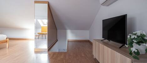 A modern room with a wooden floor, a TV on a wooden stand, and an air conditioning unit on the wall.