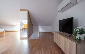 Une chambre moderne avec un plancher en bois, un téléviseur posé sur un meuble en bois et un climatiseur fixé au mur.