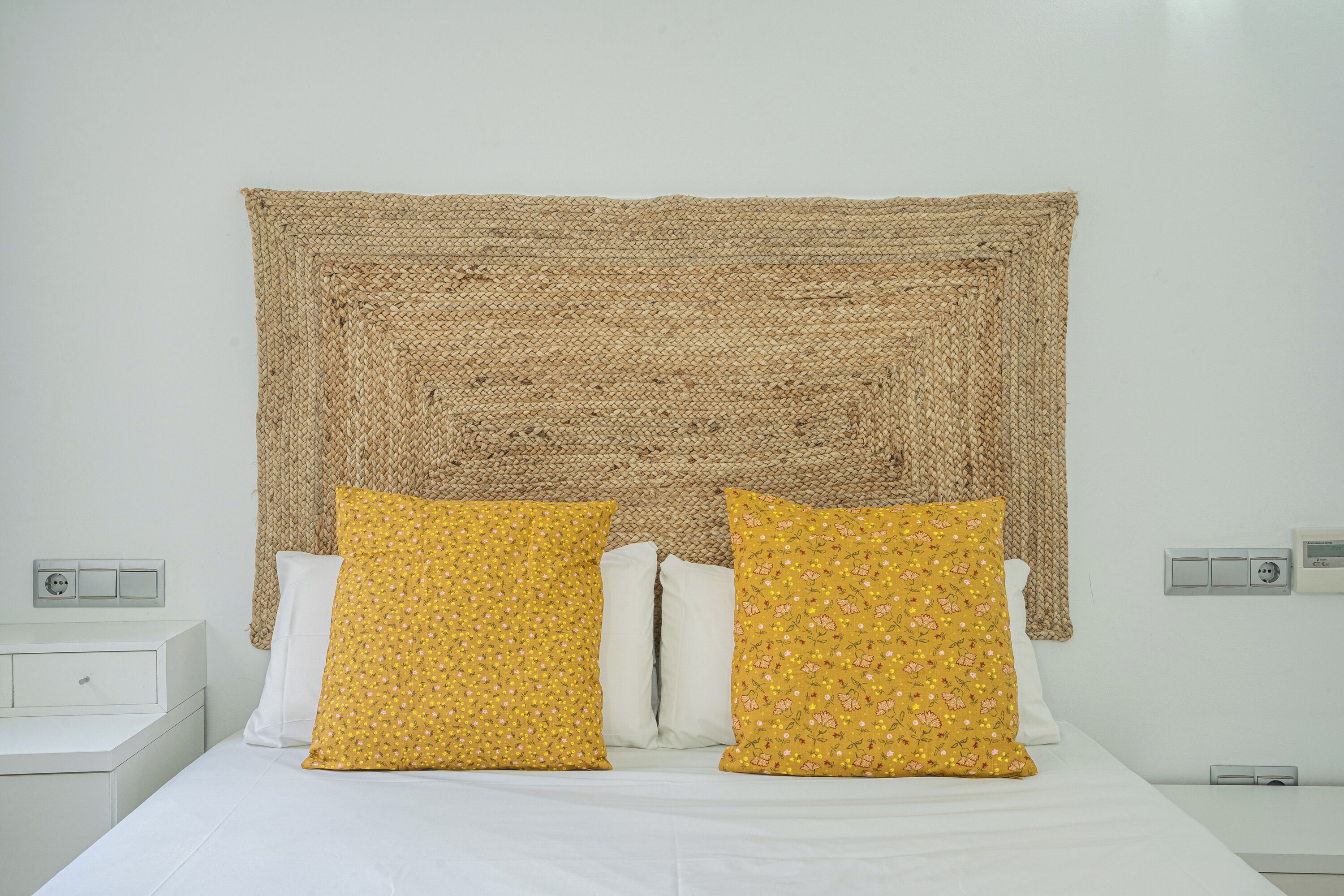 Ein Bett mit weißer Bettwäsche und zwei gelben Kissen mit Blumenmuster.
