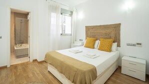 A bedroom with a large bed, a bedside table, a nightstand, a woven headboard, and a shower area. - Stay U-nique Apartment Trinidad (Málaga)