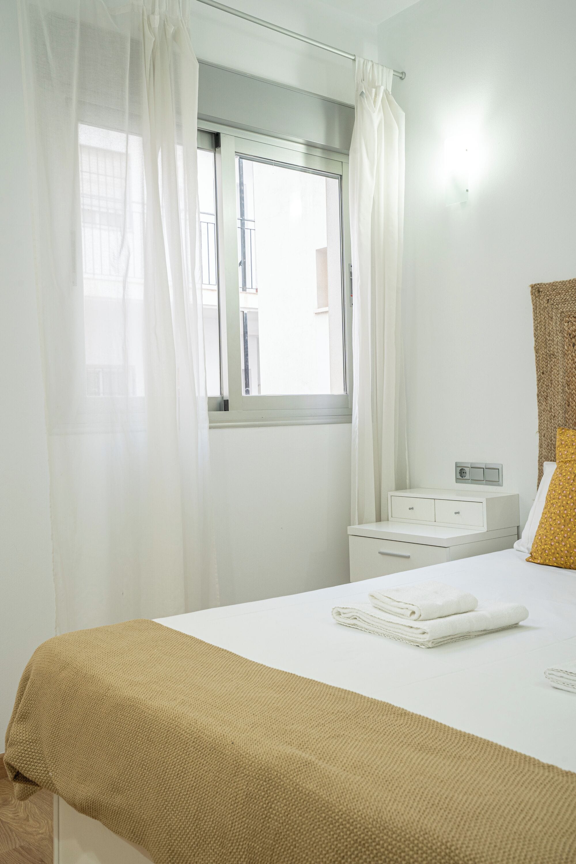 Ein Hotelzimmer mit Bett, Nachttisch, einem Fenster mit Vorhängen und einer Wandleuchte.